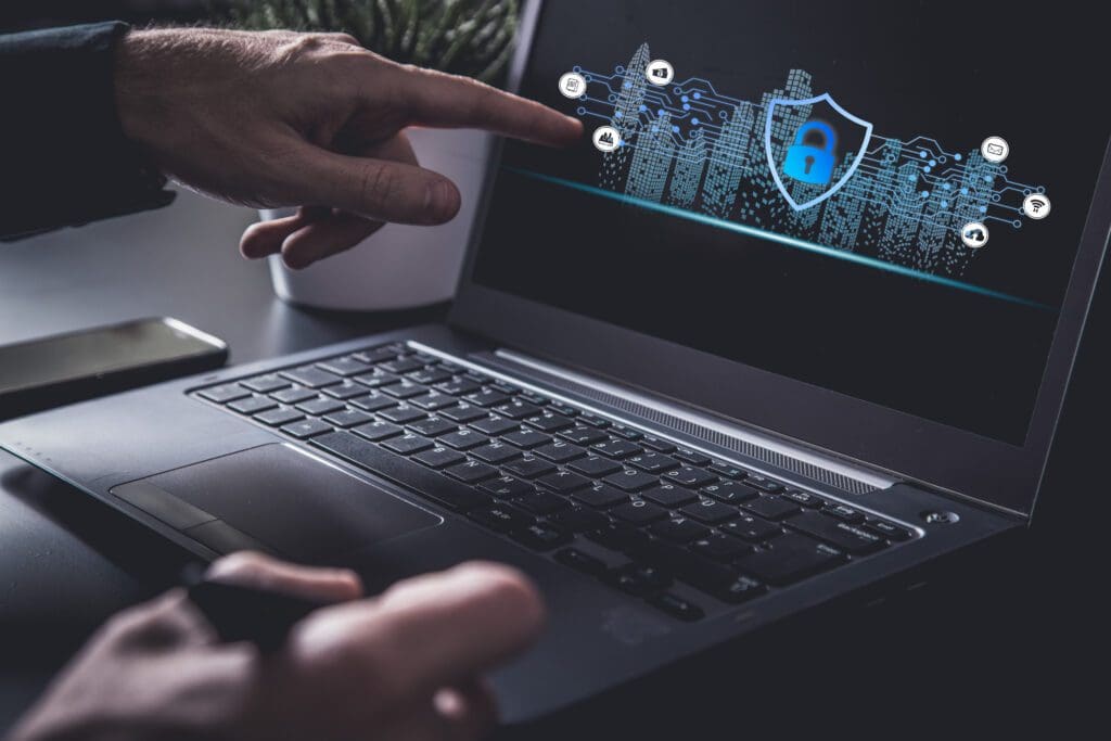 A laptop screen with cybersecurity icons and someone’s index finger pointing at the screen.