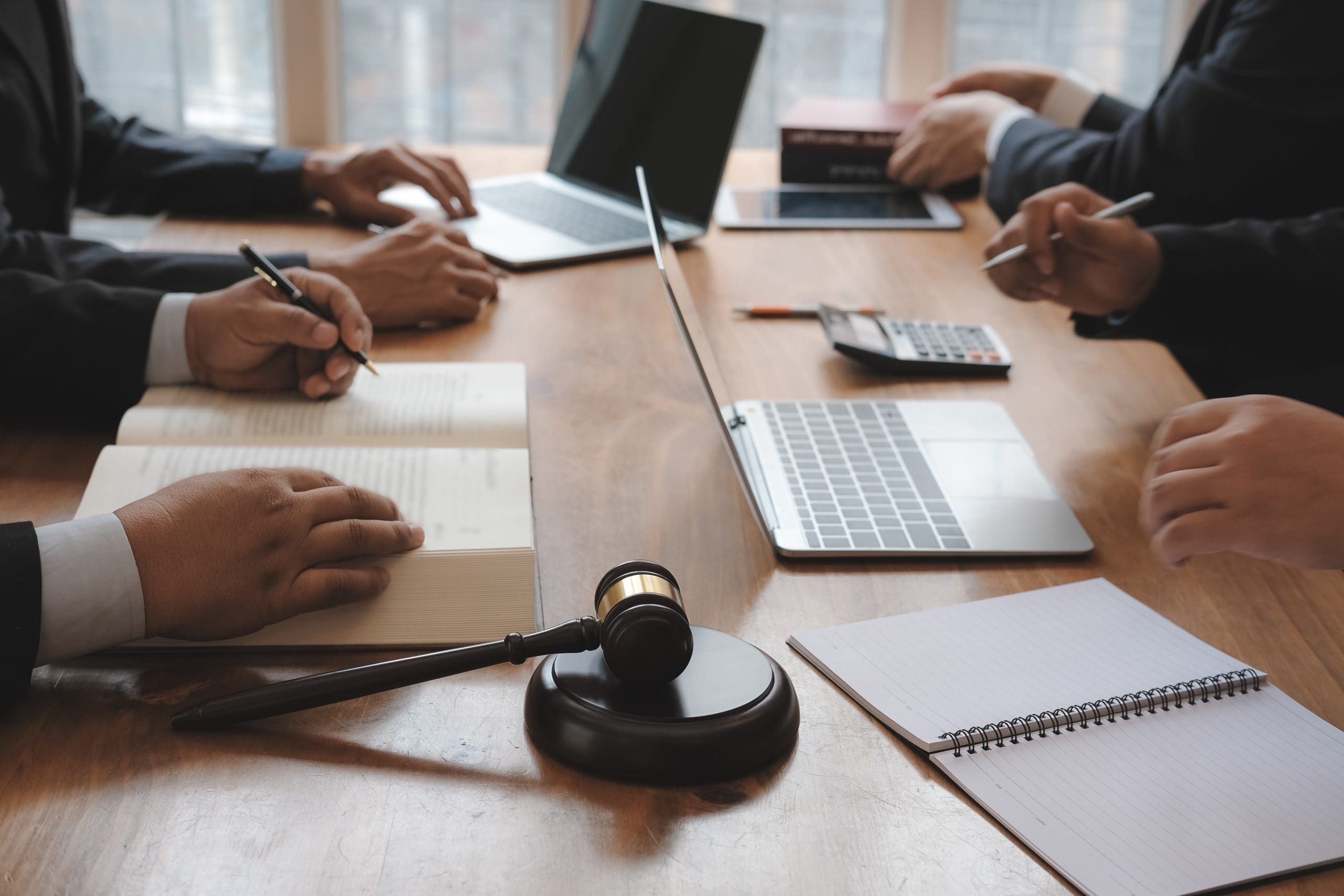 A group of lawyers around a table discuss work over laptops and tablets