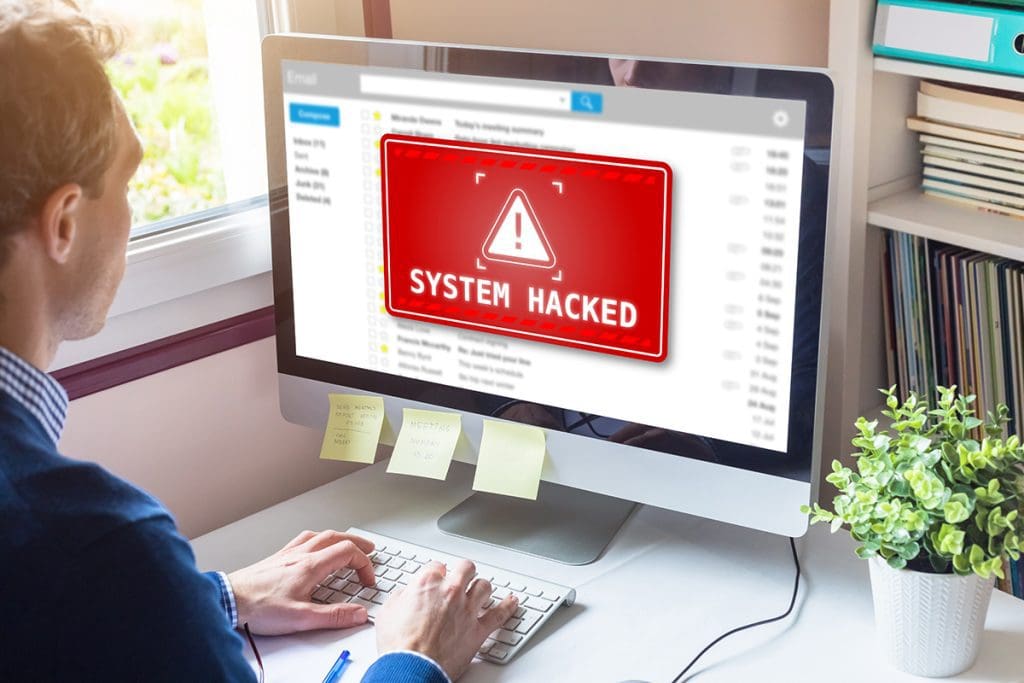 A person working on a computer with a big red warning box that reads ‘system hacked.’