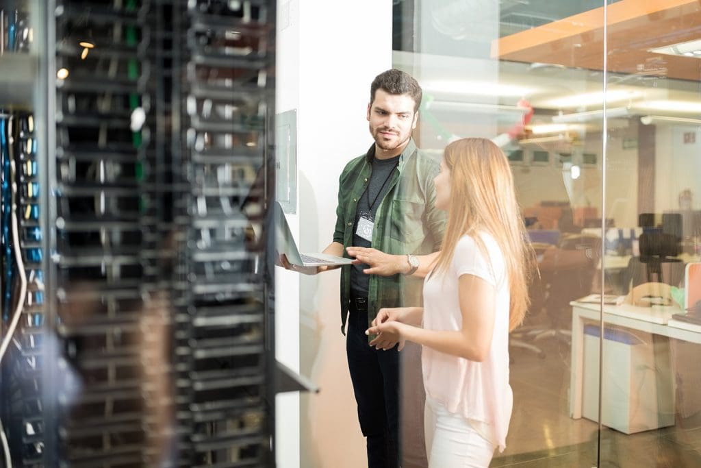 A man and women pair of colleagues who are discussing work in a server room